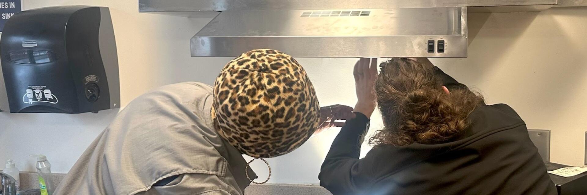Two maintenance staff are working to fix an issue with a range hood